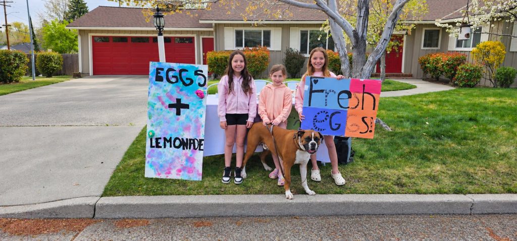 Willy the boxer standing with three children beside their egg and lemonade stand.